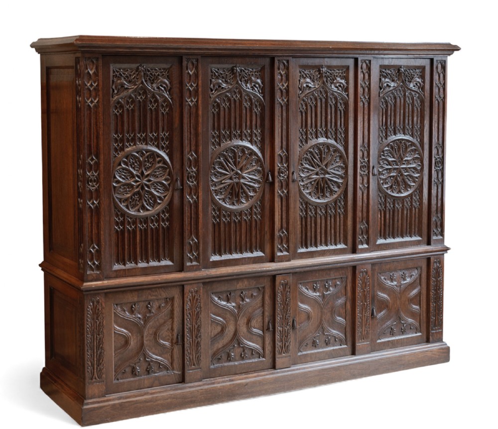 A large dark oak Gothic Revival cupboard featuring carved tracery panels, rose window motifs, and lower cabinet doors. View IX