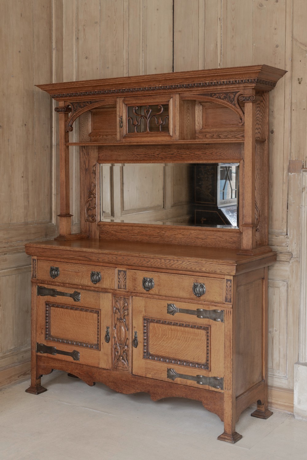 An antique Art Nouveau oak dresser featuring a mirrored upper tier with carved accents and a lower cabinet base with iron hardware.
