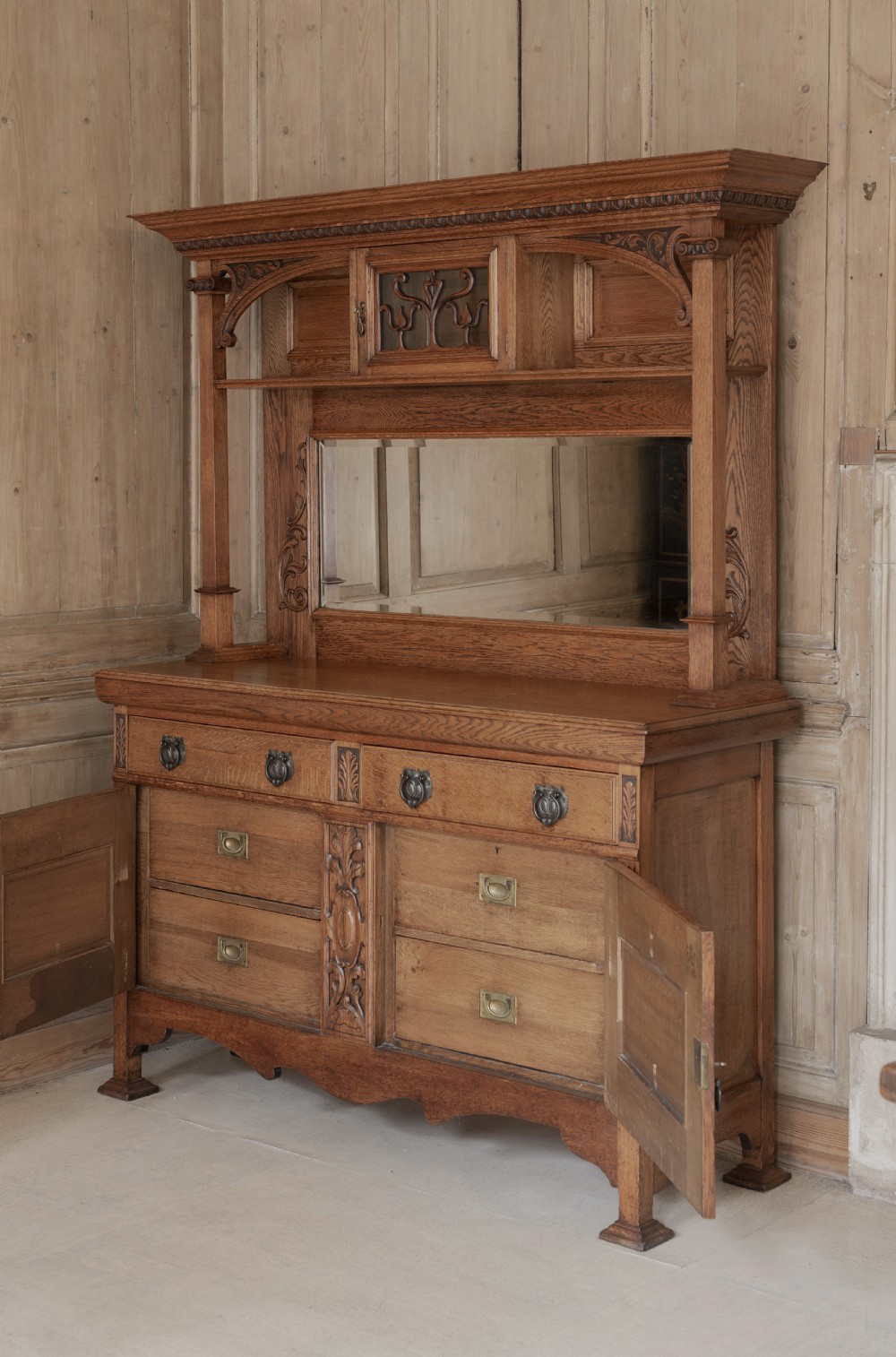 An antique Art Nouveau oak dresser featuring a mirrored upper tier with carved accents and a lower cabinet base with iron hardware. View II
