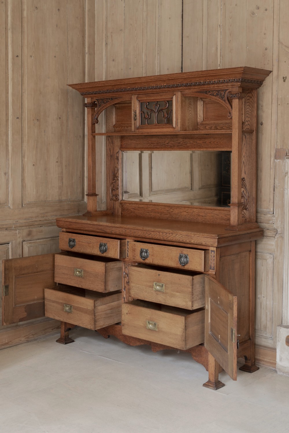 An antique Art Nouveau oak dresser featuring a mirrored upper tier with carved accents and a lower cabinet base with iron hardware. View III