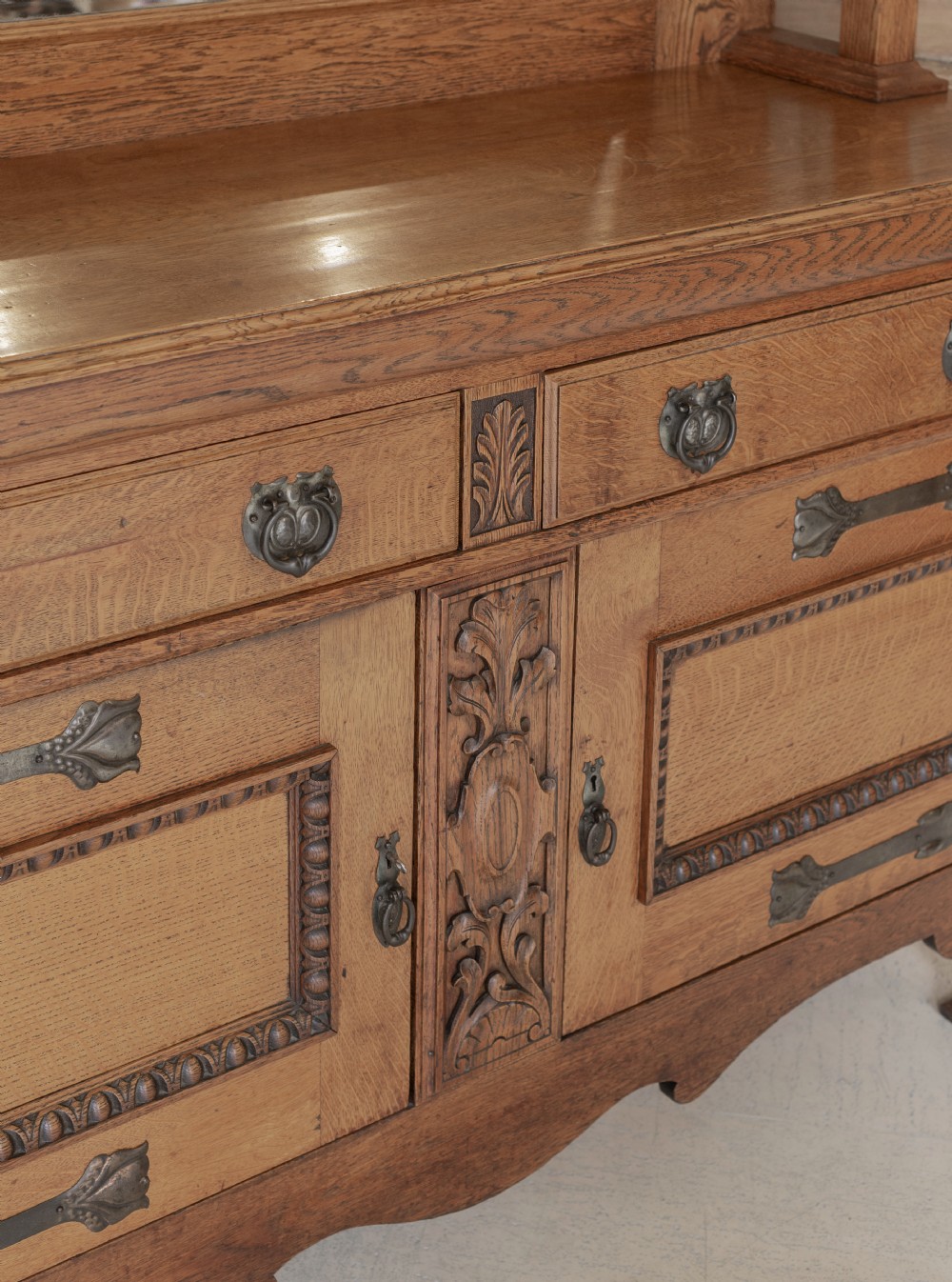 An antique Art Nouveau oak dresser featuring a mirrored upper tier with carved accents and a lower cabinet base with iron hardware. View V
