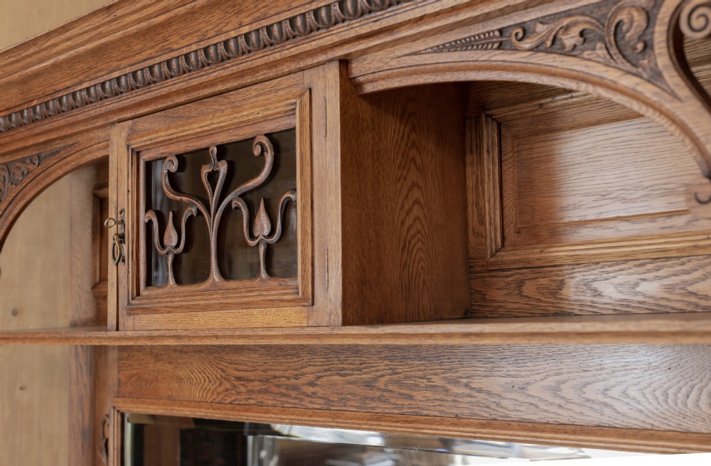 An antique Art Nouveau oak dresser featuring a mirrored upper tier with carved accents and a lower cabinet base with iron hardware. View VII