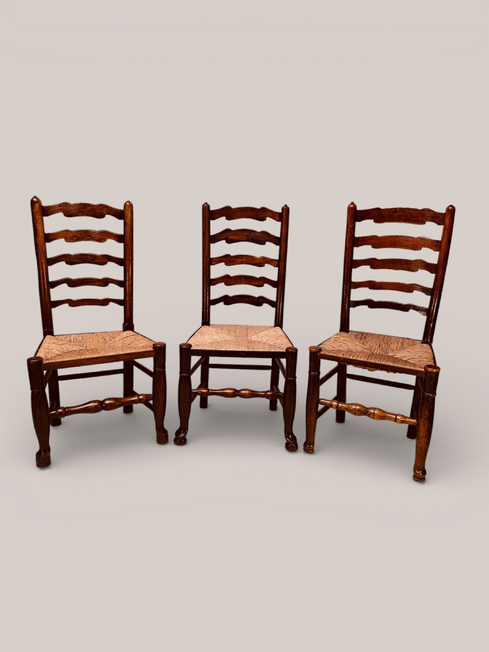 A pair of dark ash carver dining chairs featuring shaped wavy ladderback slats, turned front legs, and woven rush seats. View II