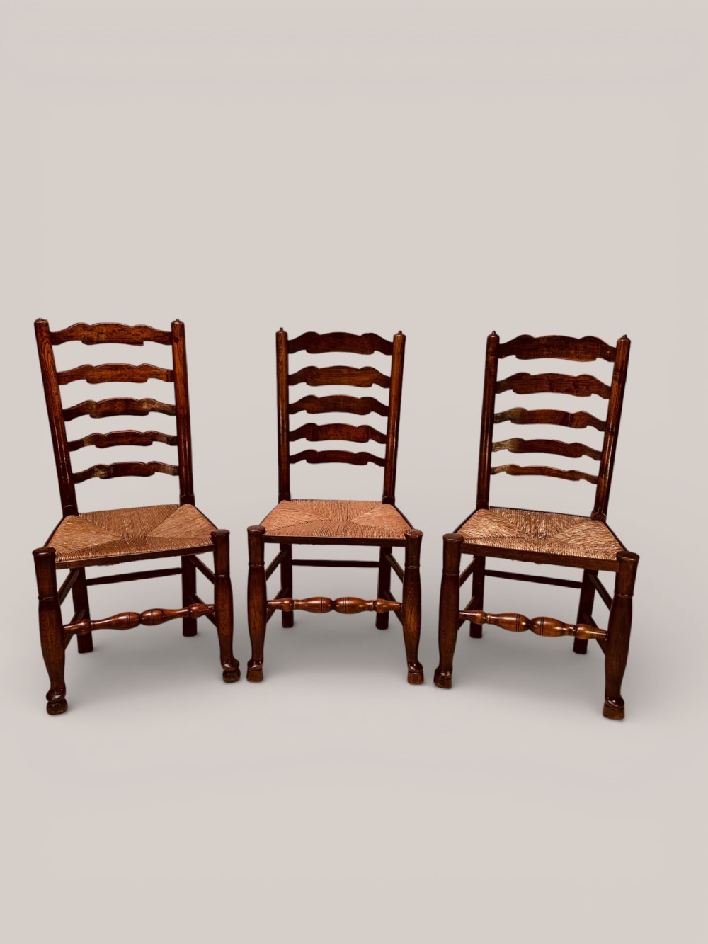 A pair of dark ash carver dining chairs featuring shaped wavy ladderback slats, turned front legs, and woven rush seats. View III