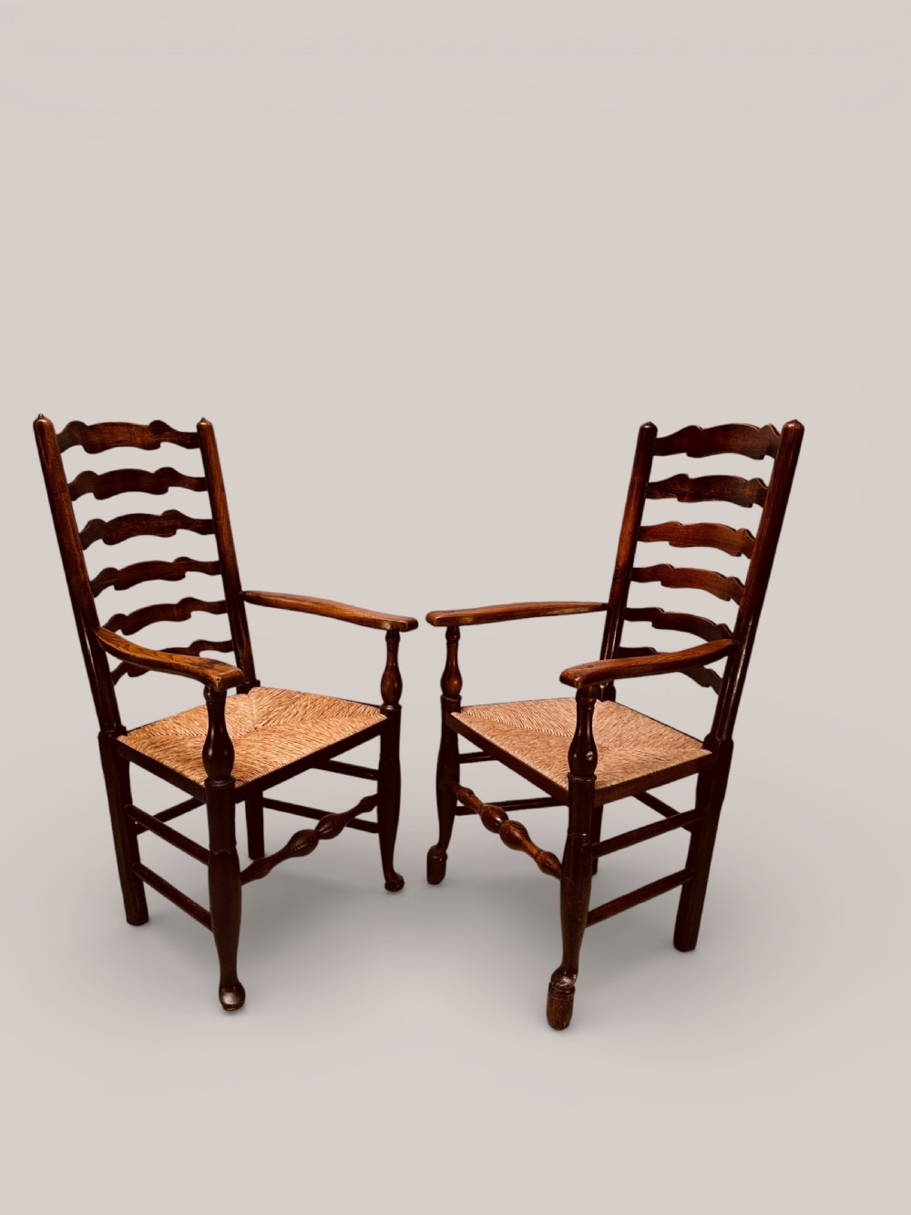 A pair of dark ash carver dining chairs featuring shaped wavy ladderback slats, turned front legs, and woven rush seats. View VII