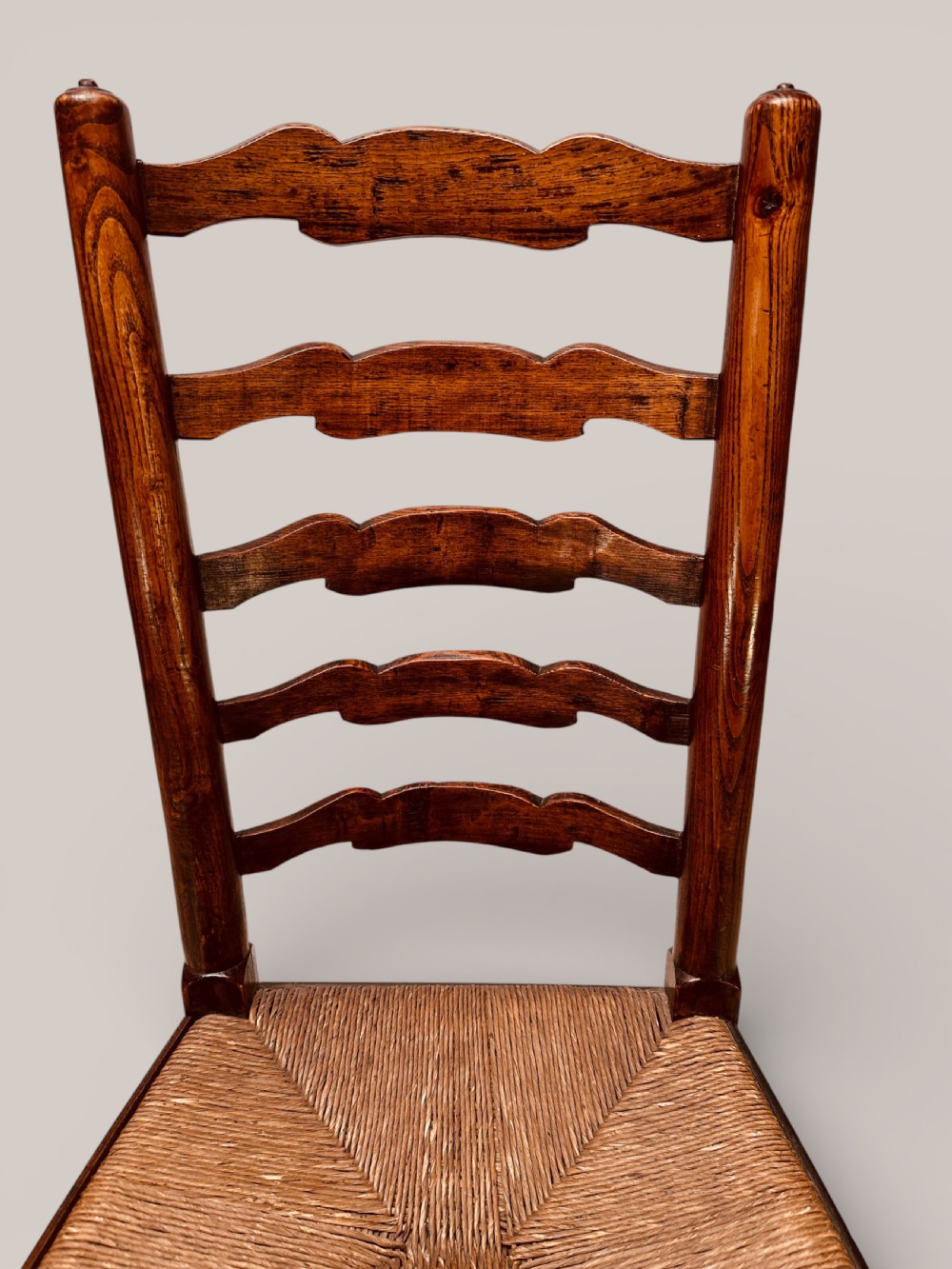 A pair of dark ash carver dining chairs featuring shaped wavy ladderback slats, turned front legs, and woven rush seats. View X
