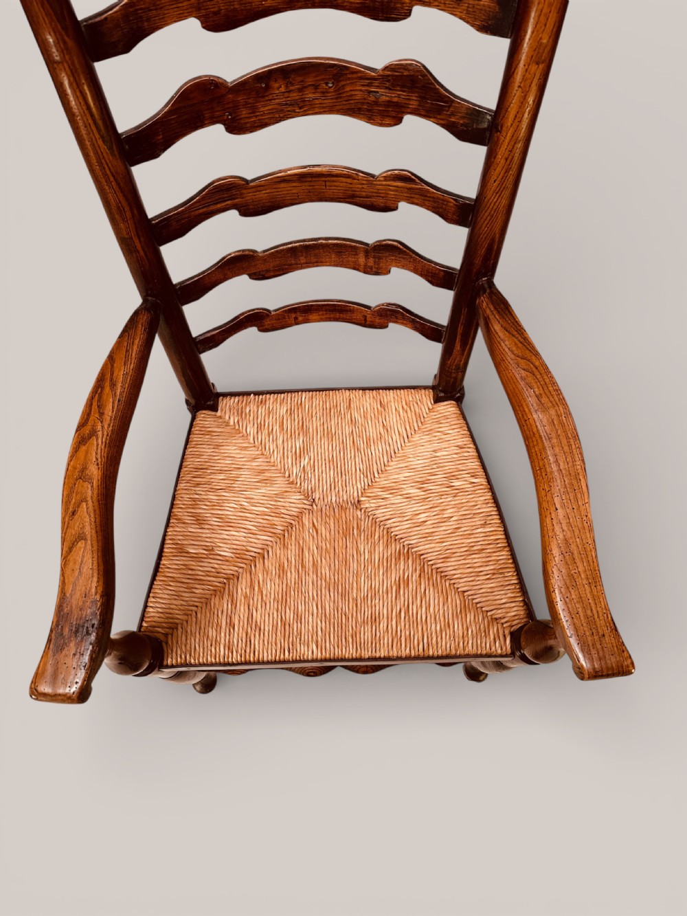 A pair of dark ash carver dining chairs featuring shaped wavy ladderback slats, turned front legs, and woven rush seats. View XI