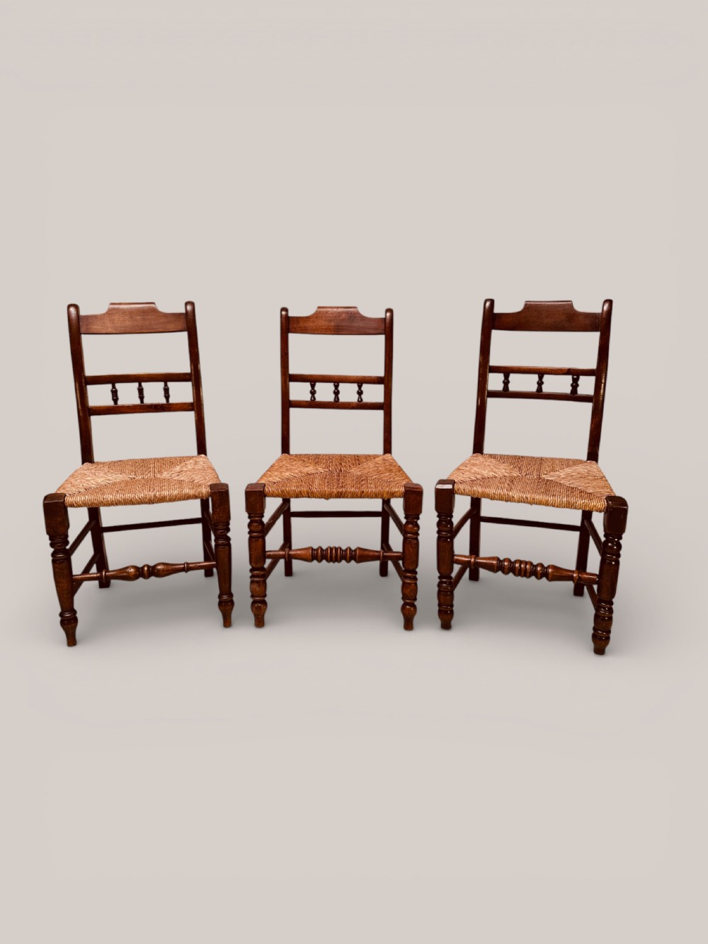 A set of dark ash and alder wood dining chairs featuring hand-woven rush seats, turned front legs, and decorative back spindles.