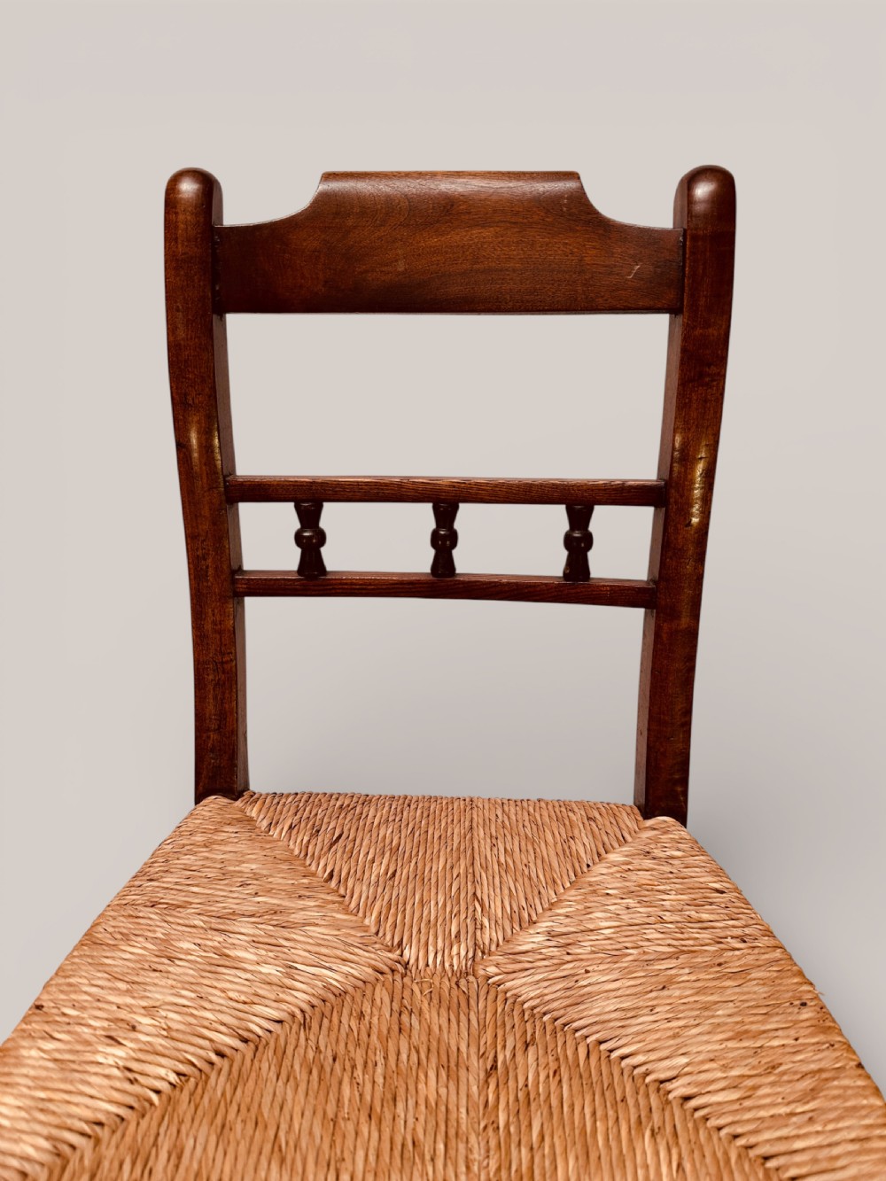 A set of dark ash and alder wood dining chairs featuring hand-woven rush seats, turned front legs, and decorative back spindles. View IX