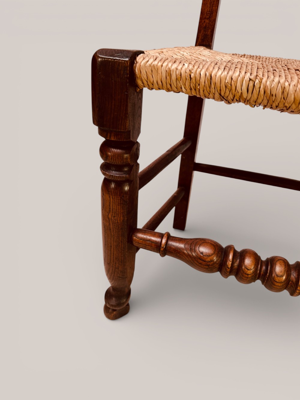A set of dark ash and alder wood dining chairs featuring hand-woven rush seats, turned front legs, and decorative back spindles. View X