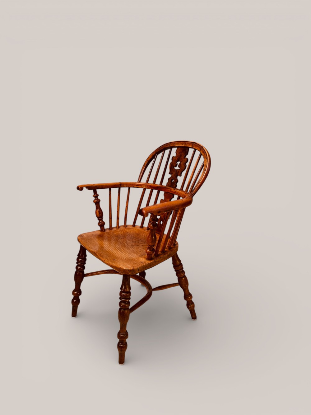 A Victorian 19th-century Windsor low back armchair constructed from yew and elm wood featuring turned legs, a pierced splat, and a contoured saddle seat.