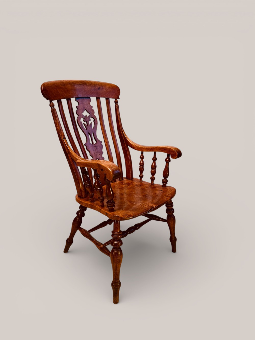 A Victorian Windsor armchair crafted from beech and elm with a pierced back splat, turned legs, and curved armrests.