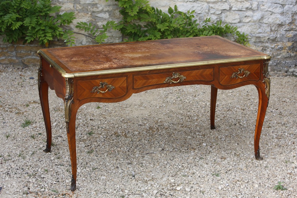 A Louis XV style bureau plat writing desk crafted from rosewood and tulipwood parquetry veneer, featuring gilt-bronze mounts, cabriole legs, three frieze drawers, and a leather-inset writing top.