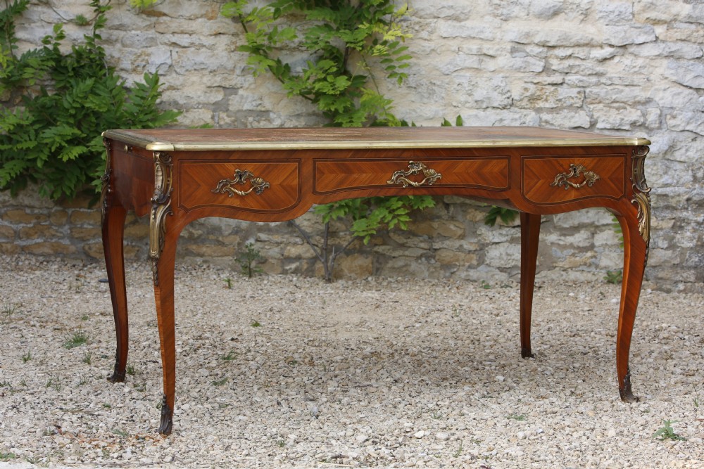 A Louis XV style bureau plat writing desk crafted from rosewood and tulipwood parquetry veneer, featuring gilt-bronze mounts, cabriole legs, three frieze drawers, and a leather-inset writing top. View II