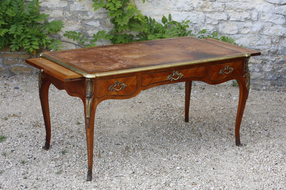 A Louis XV style bureau plat writing desk crafted from rosewood and tulipwood parquetry veneer, featuring gilt-bronze mounts, cabriole legs, three frieze drawers, and a leather-inset writing top. View X