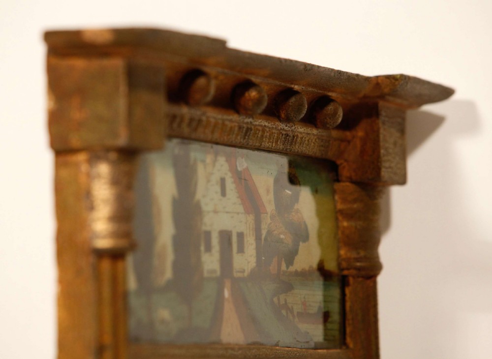 An antique Regency giltwood pier mirror featuring fluted side columns, a sphere-ornamented upper cornice, and a reverse-painted landscape scene on the top panel. View VI