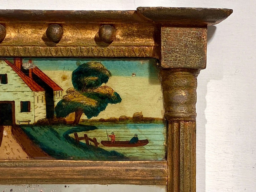 An antique Regency giltwood pier mirror featuring fluted side columns, a sphere-ornamented upper cornice, and a reverse-painted landscape scene on the top panel. View X
