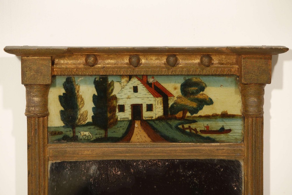 An antique Regency giltwood pier mirror featuring fluted side columns, a sphere-ornamented upper cornice, and a reverse-painted landscape scene on the top panel. View XXIX