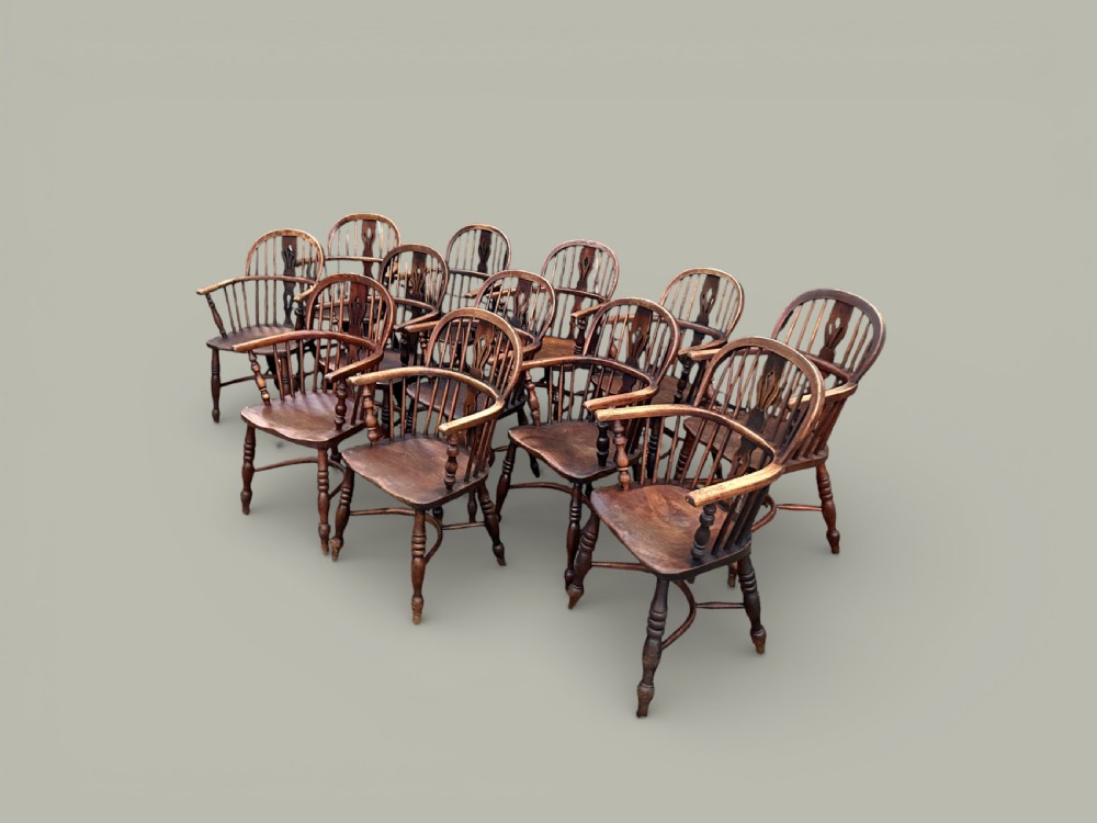 A set of twelve antique low back Windsor armchairs crafted from warm brown ash and elm with turned legs and hoop backs.