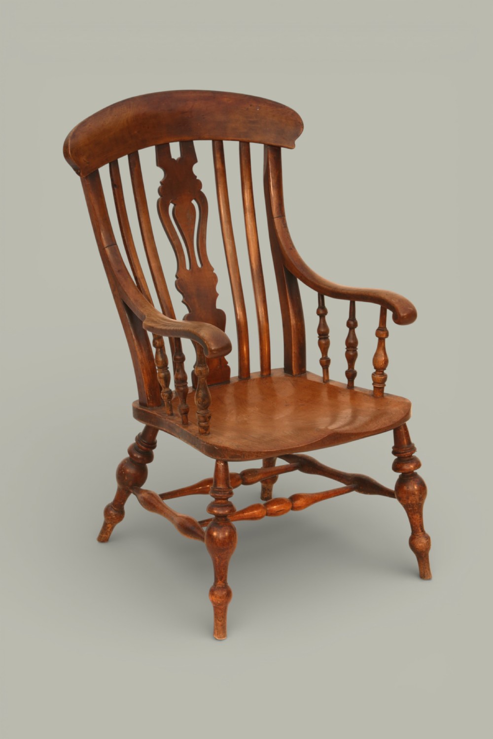A late nineteenth-century British Windsor armchair made of warm brown elm and fruitwood with a shaped crest rail, pierced central splat, turned spindles, contoured saddle seat, and turned legs with stretchers.