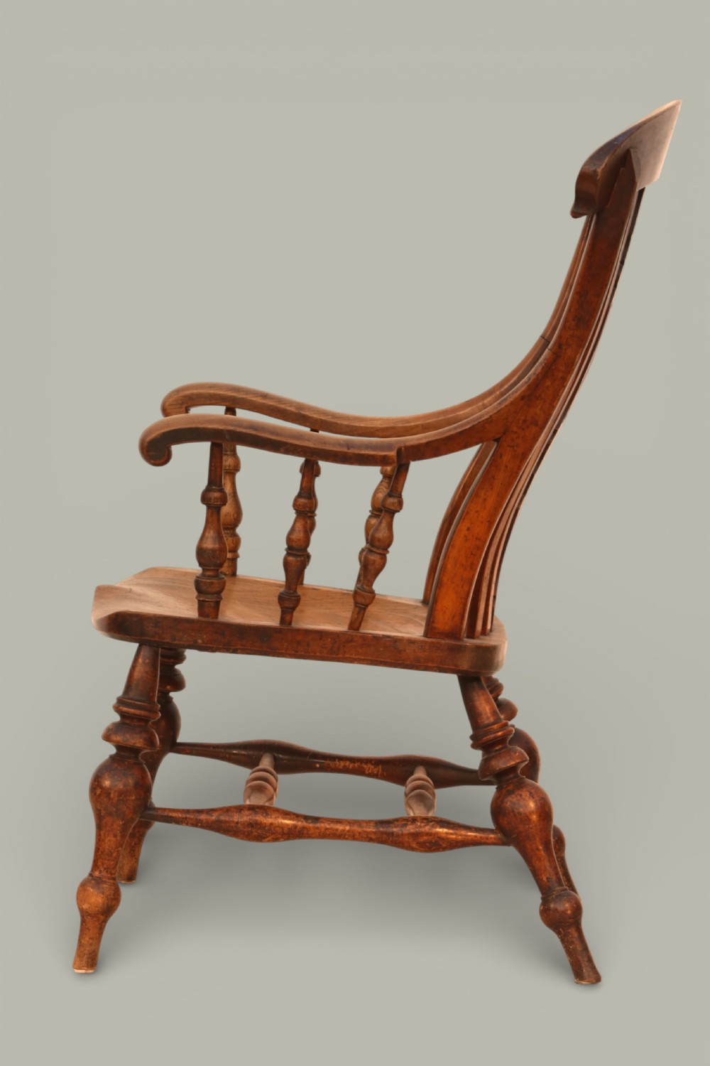 A late nineteenth-century British Windsor armchair made of warm brown elm and fruitwood with a shaped crest rail, pierced central splat, turned spindles, contoured saddle seat, and turned legs with stretchers. View IV