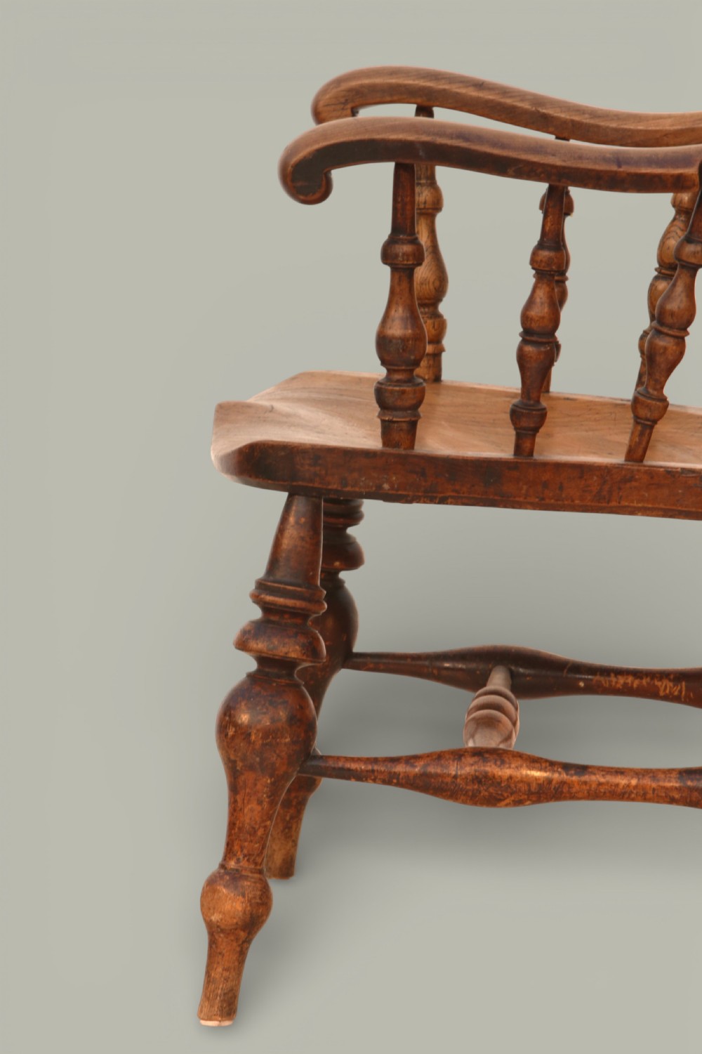 A late nineteenth-century British Windsor armchair made of warm brown elm and fruitwood with a shaped crest rail, pierced central splat, turned spindles, contoured saddle seat, and turned legs with stretchers. View V