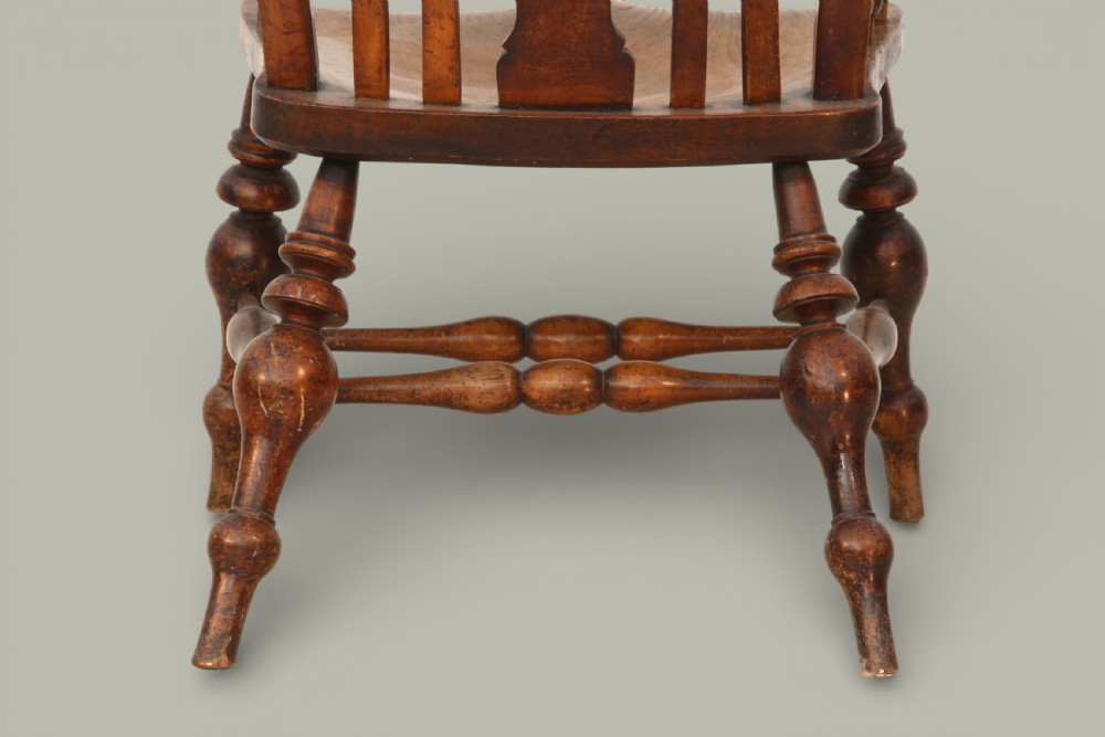 A late nineteenth-century British Windsor armchair made of warm brown elm and fruitwood with a shaped crest rail, pierced central splat, turned spindles, contoured saddle seat, and turned legs with stretchers. View X