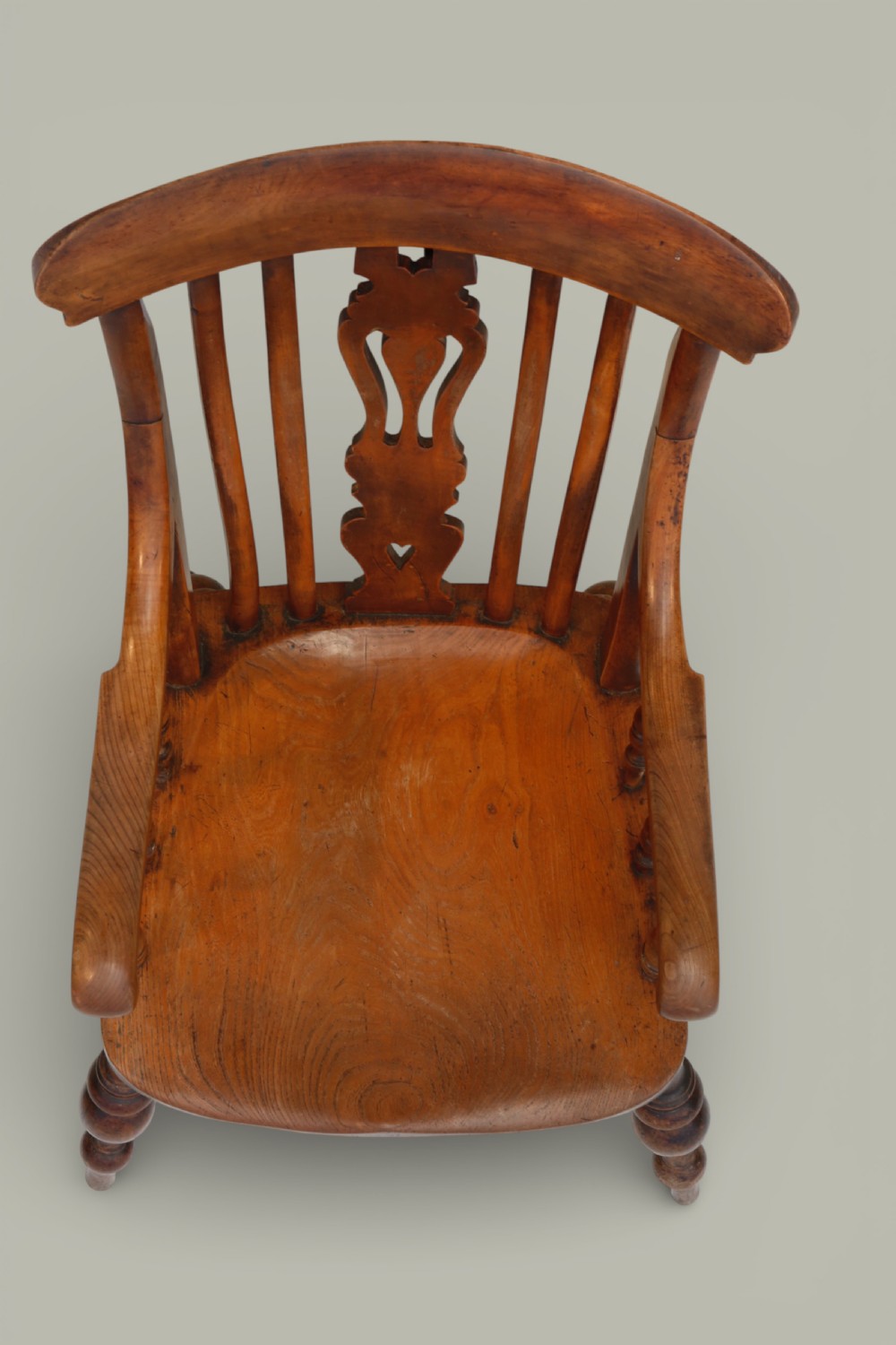 A late nineteenth-century British Windsor armchair made of warm brown elm and fruitwood with a shaped crest rail, pierced central splat, turned spindles, contoured saddle seat, and turned legs with stretchers. View XI