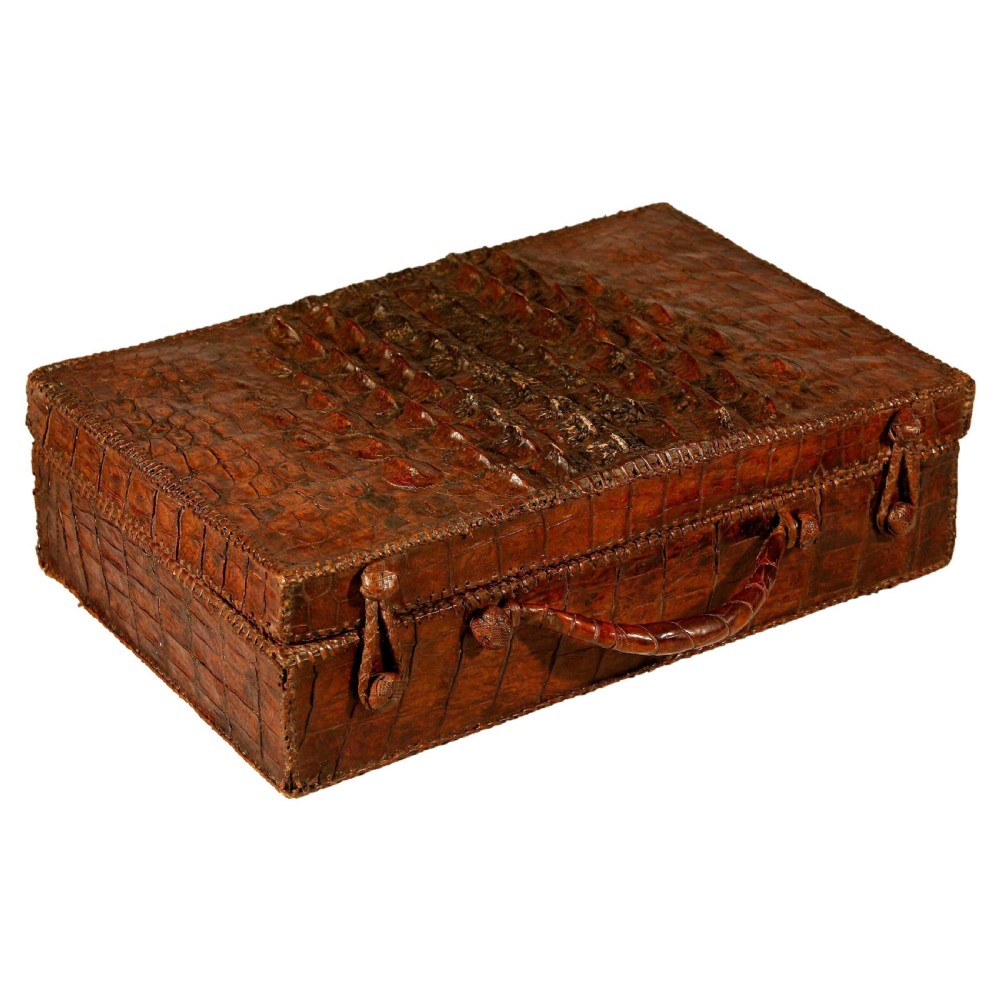 A rectangular warm brown hornback crocodile leather suitcase with prominent dorsal ridges, stitched edging, and a central leather carrying handle.
