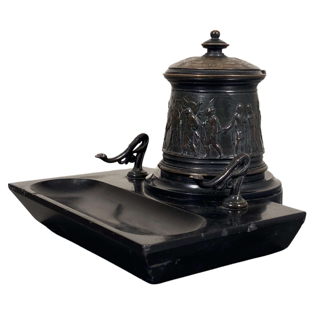 A Neoclassical patinated bronze inkwell featuring relief classical figures mounted on a black marble base with an integrated pen rest.