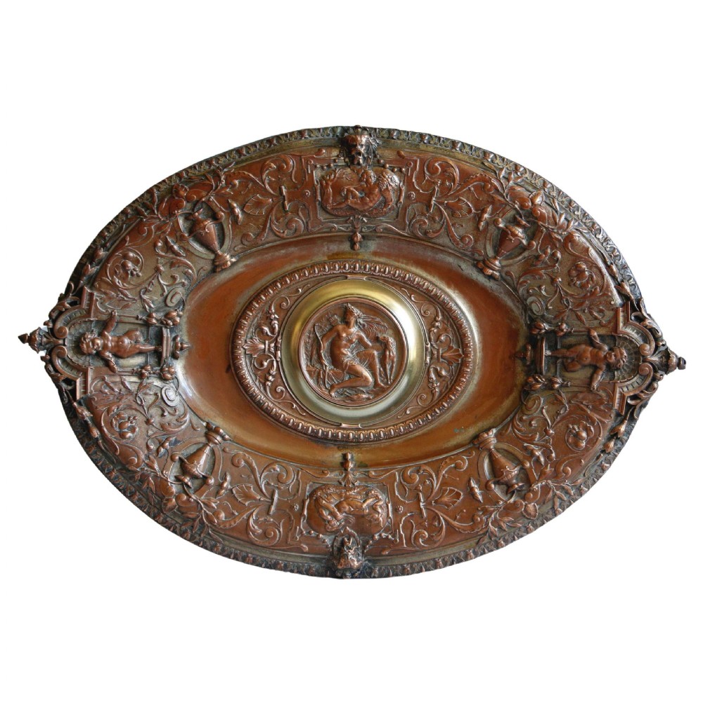 An oval 19th-century copper and brass relief dish featuring a central medallion of Diana the Huntress surrounded by intricate cherub and scrollwork motifs.