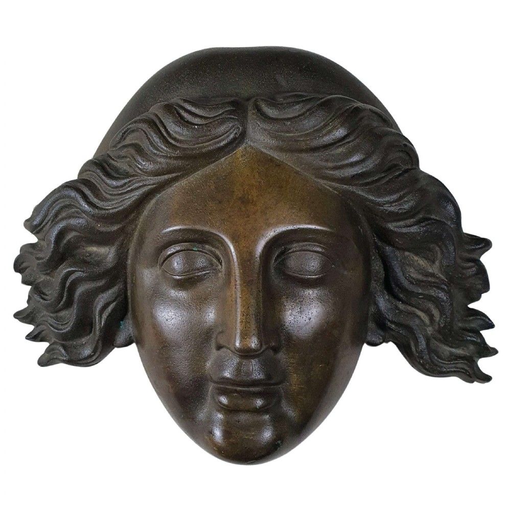 A dark patinated bronze head sculpture of a classical female face with symmetrical features and stylized wavy hair.