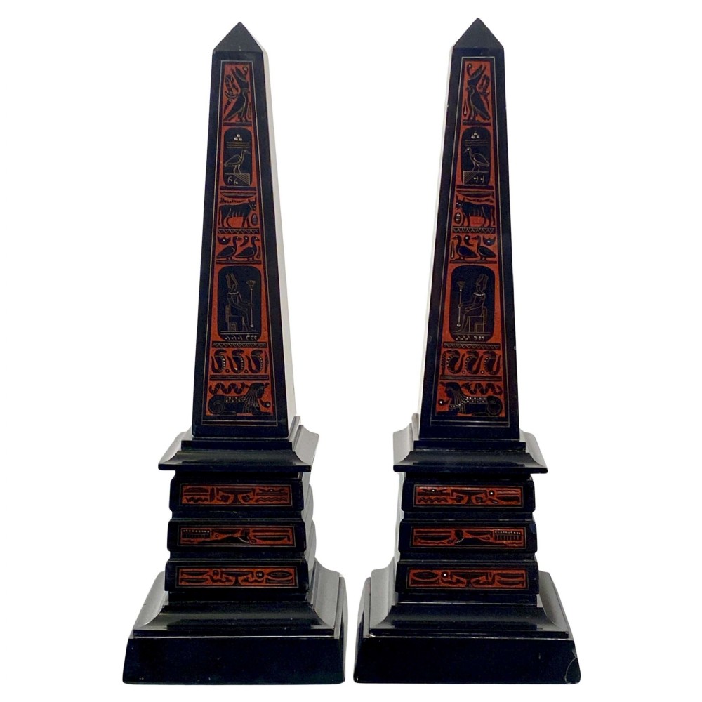 A pair of black marble obelisks featuring etched Egyptian hieroglyphs filled with red terracotta-coloured pigment on stepped plinth bases.