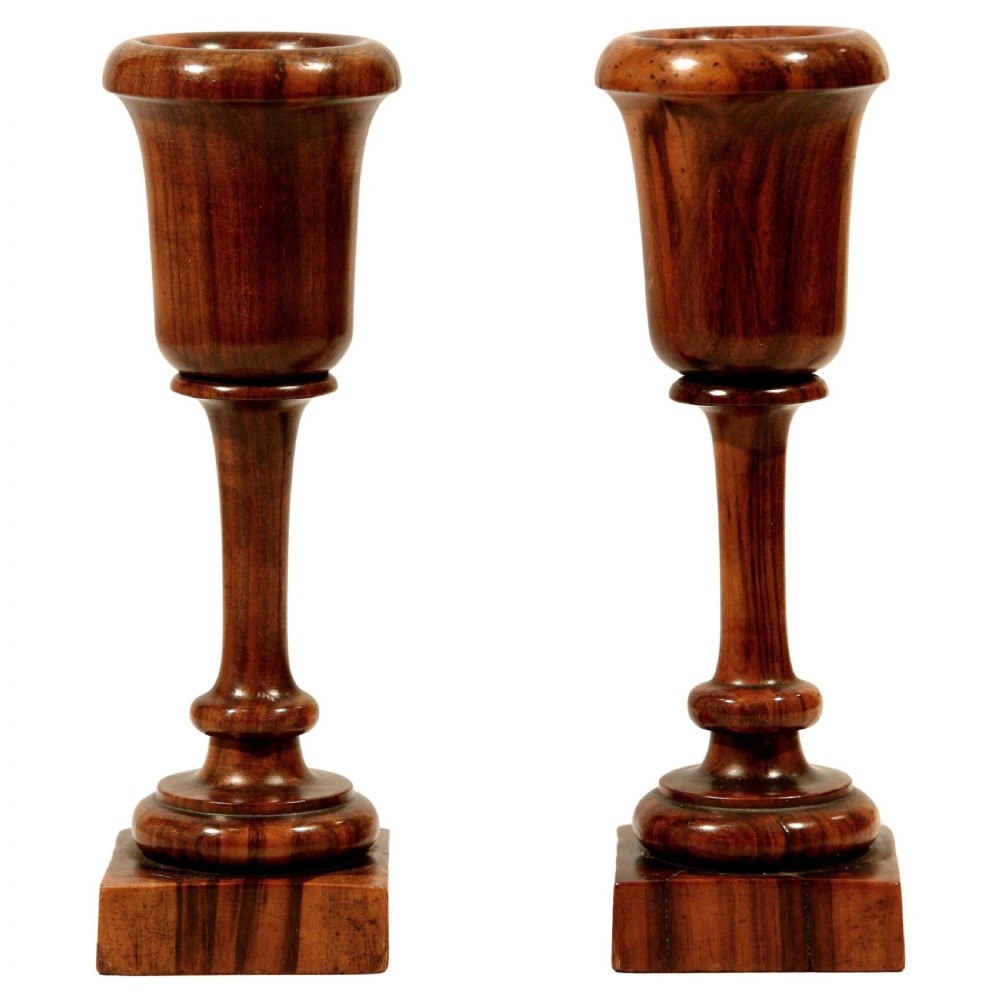A pair of turned dark brown lignum vitae wood spill vases featuring urn-shaped cups, slender pedestals, and square bases.