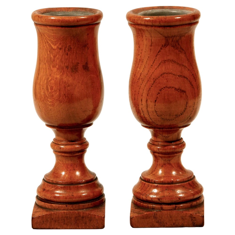 A pair of turned oak wooden spill vases shaped like urns with metal rim liners on square plinth bases.