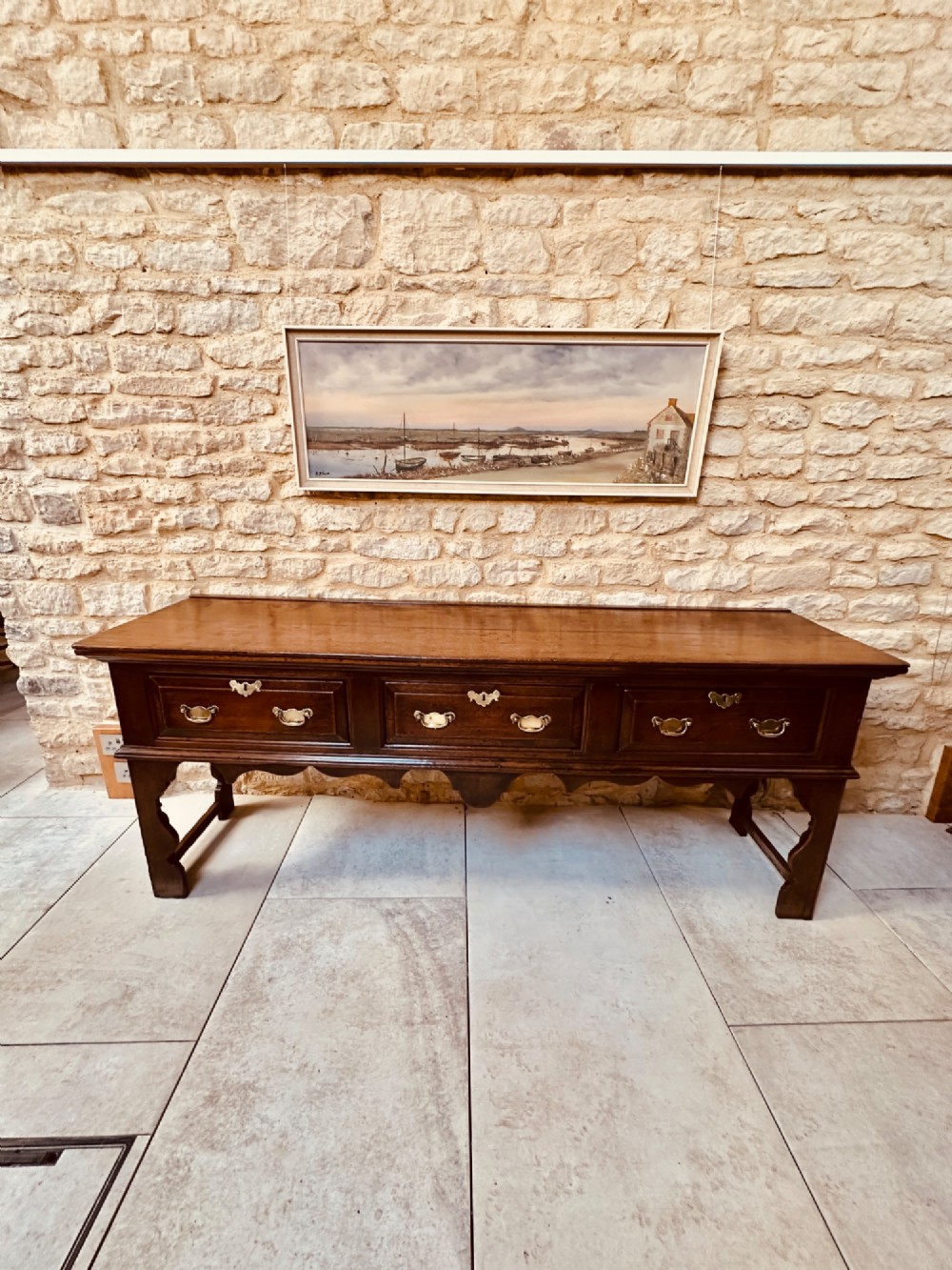 An 18th-century dark oak dresser base featuring three drawers with brass handles and shaped silhouette legs.