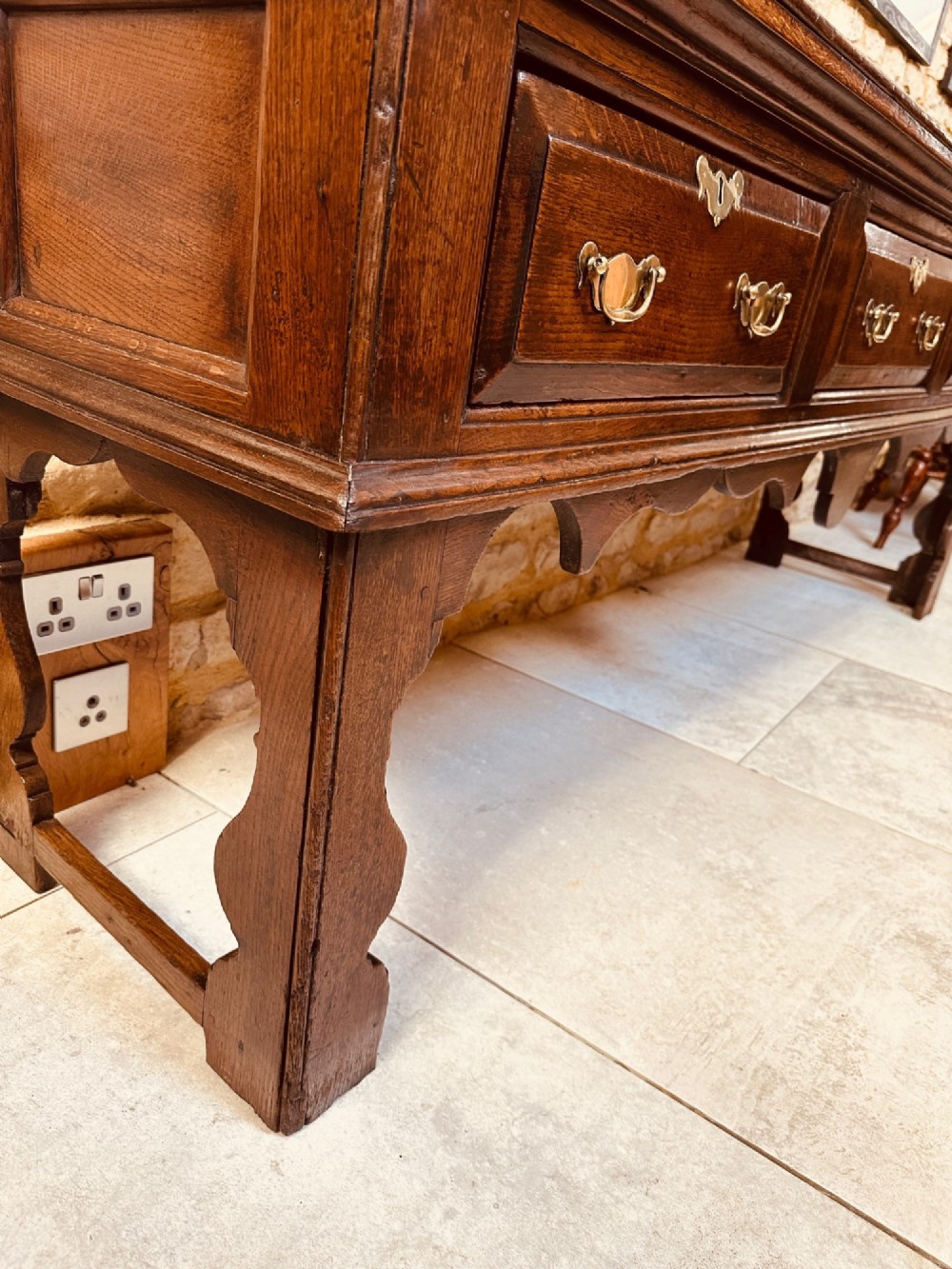 An 18th-century dark oak dresser base featuring three drawers with brass handles and shaped silhouette legs. View III