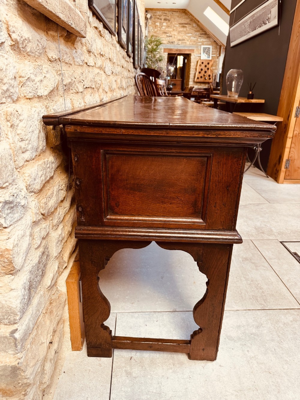 An 18th-century dark oak dresser base featuring three drawers with brass handles and shaped silhouette legs. View VI