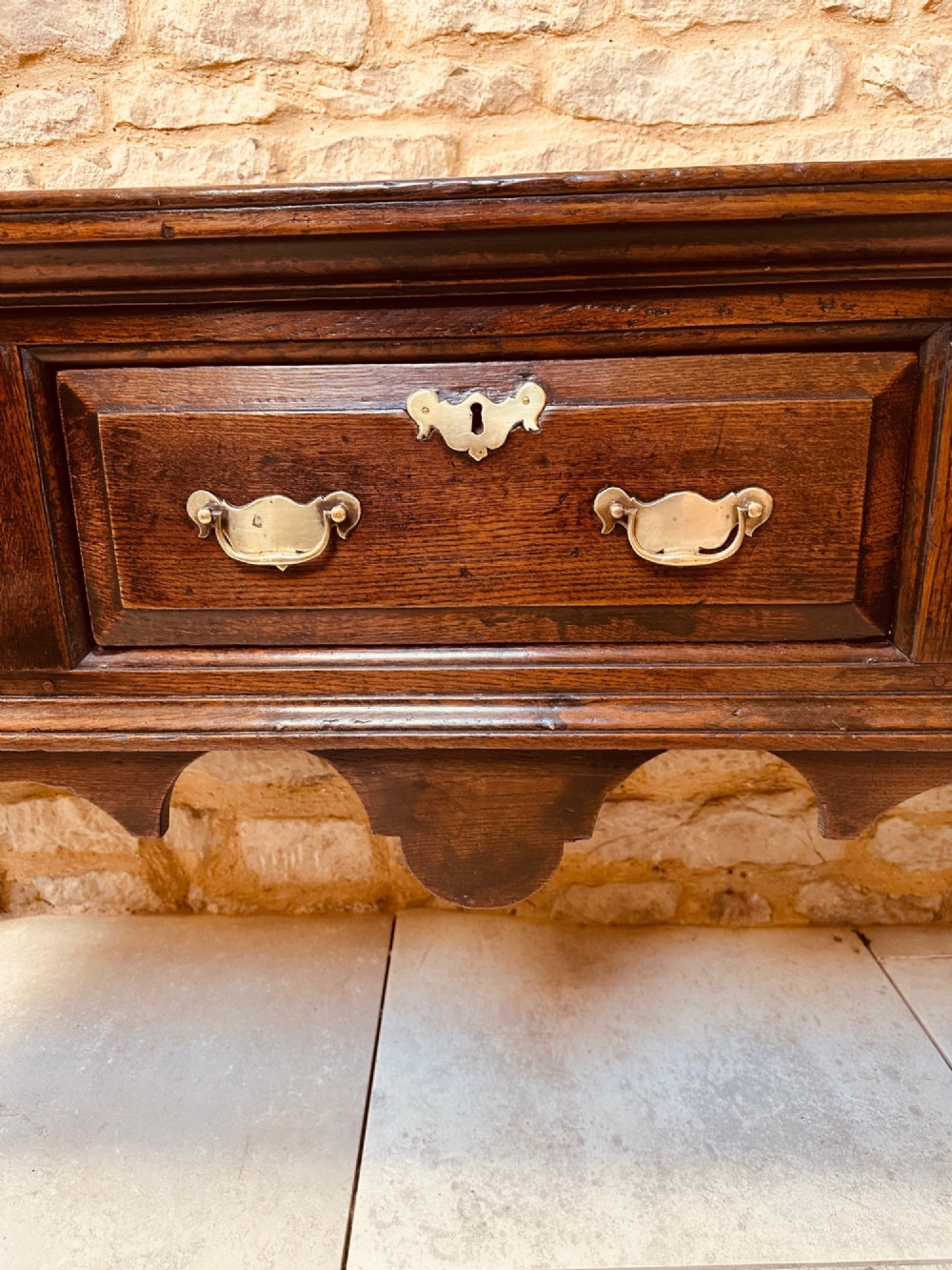 An 18th-century dark oak dresser base featuring three drawers with brass handles and shaped silhouette legs. View VII