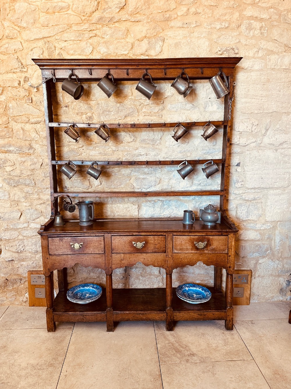 An 18th-century oak potboard dresser featuring an upper open rack with multiple shelves and cup hooks above three frieze drawers and an open lower potboard shelf.