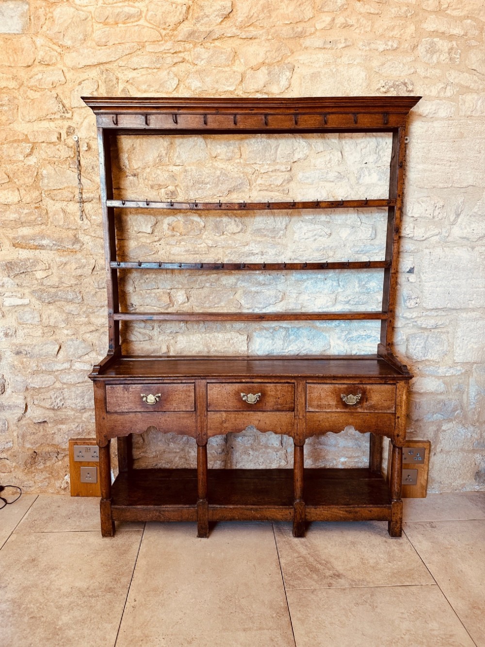 An 18th-century oak potboard dresser featuring an upper open rack with multiple shelves and cup hooks above three frieze drawers and an open lower potboard shelf. View II