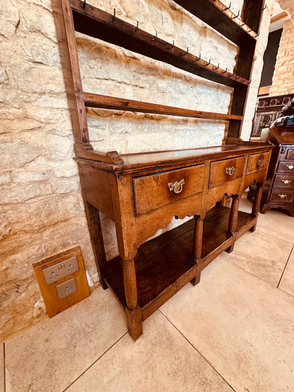 An 18th-century oak potboard dresser featuring an upper open rack with multiple shelves and cup hooks above three frieze drawers and an open lower potboard shelf. View IV