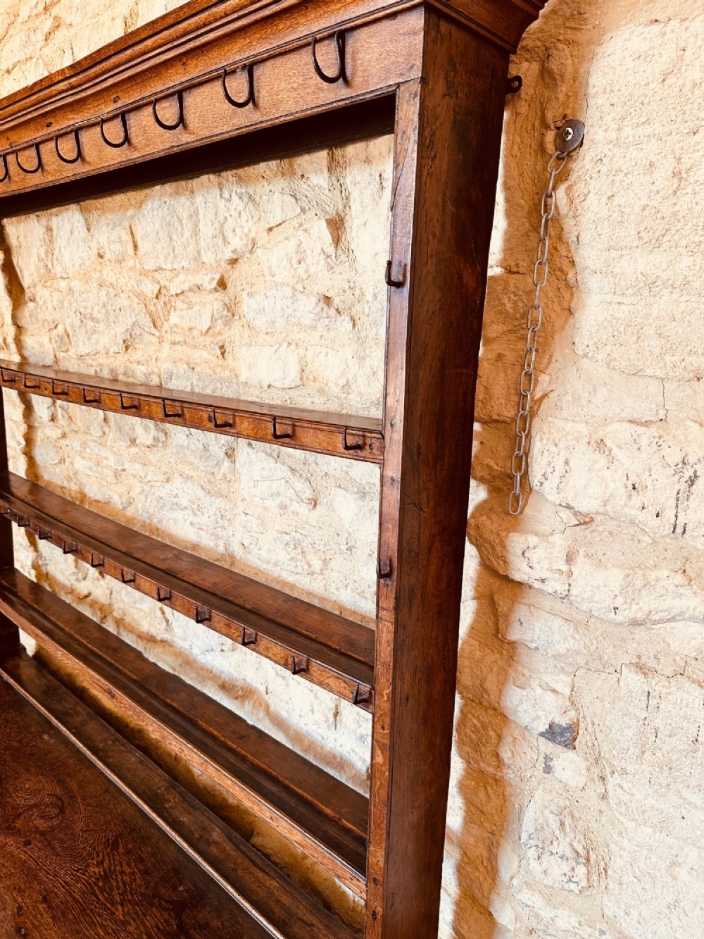 An 18th-century oak potboard dresser featuring an upper open rack with multiple shelves and cup hooks above three frieze drawers and an open lower potboard shelf. View VI