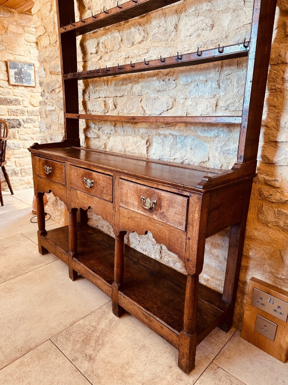 An 18th-century oak potboard dresser featuring an upper open rack with multiple shelves and cup hooks above three frieze drawers and an open lower potboard shelf. View VIII