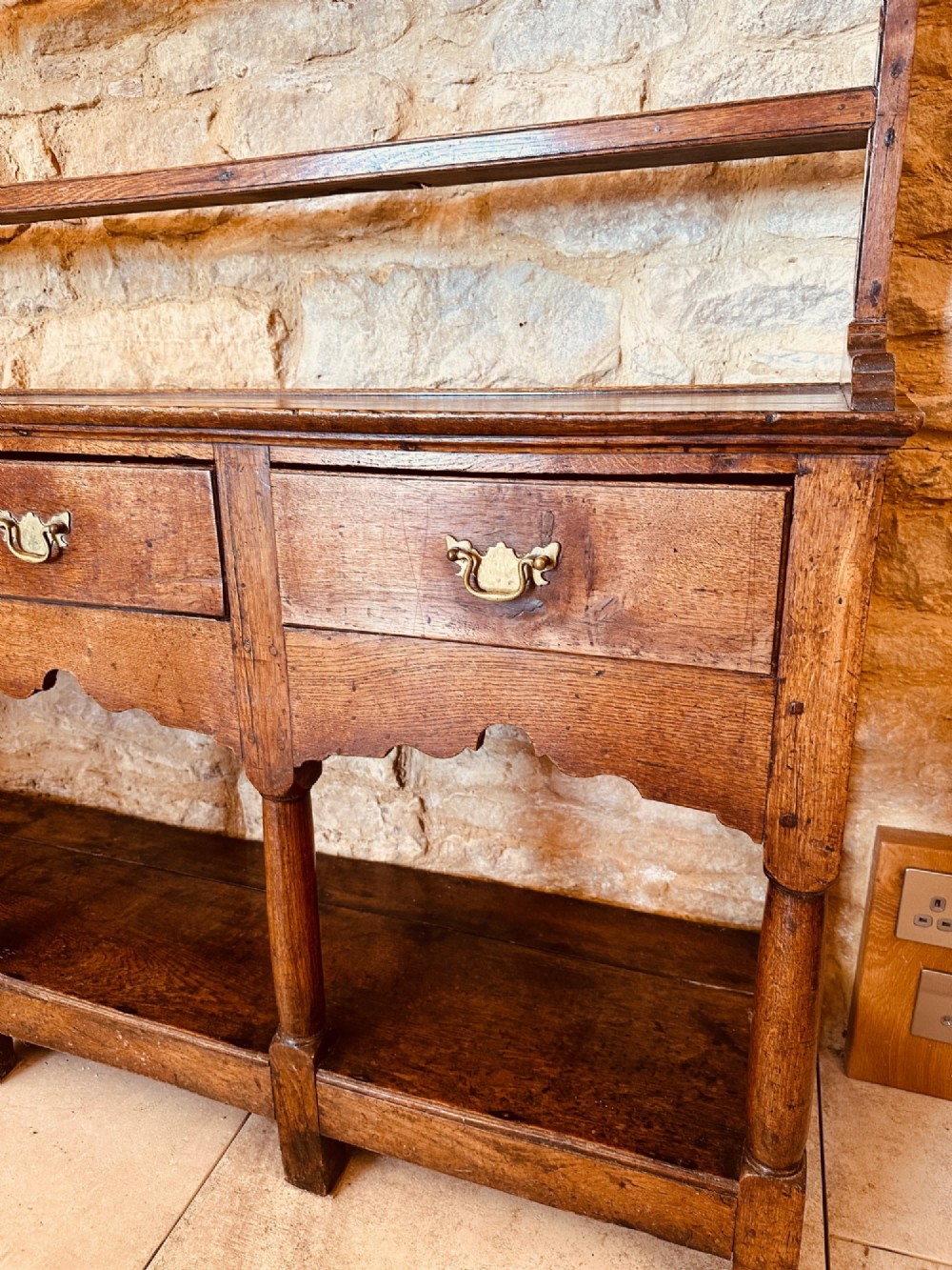 An 18th-century oak potboard dresser featuring an upper open rack with multiple shelves and cup hooks above three frieze drawers and an open lower potboard shelf. View IX
