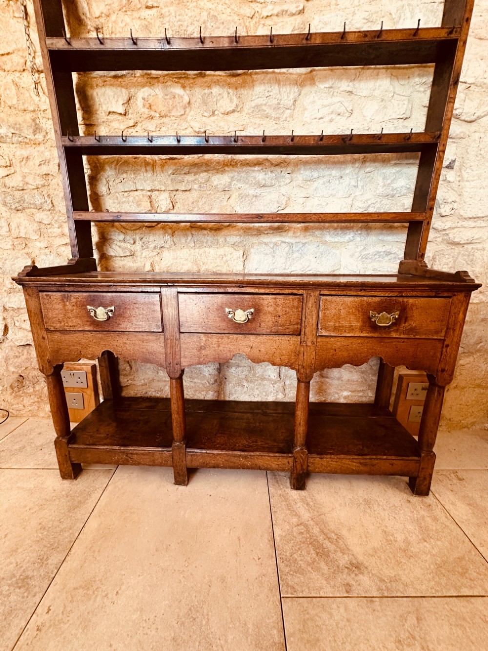 An 18th-century oak potboard dresser featuring an upper open rack with multiple shelves and cup hooks above three frieze drawers and an open lower potboard shelf. View X