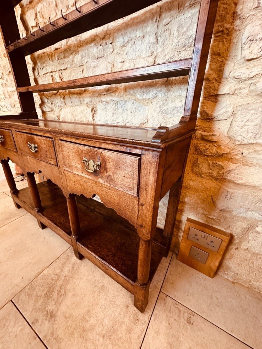 An 18th-century oak potboard dresser featuring an upper open rack with multiple shelves and cup hooks above three frieze drawers and an open lower potboard shelf. View XII