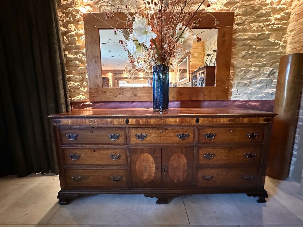 A Georgian oak Lancashire dresser base circa 1800 featuring drawer configuration, central cupboard doors with oval mahogany inlays, and brass handles. View II