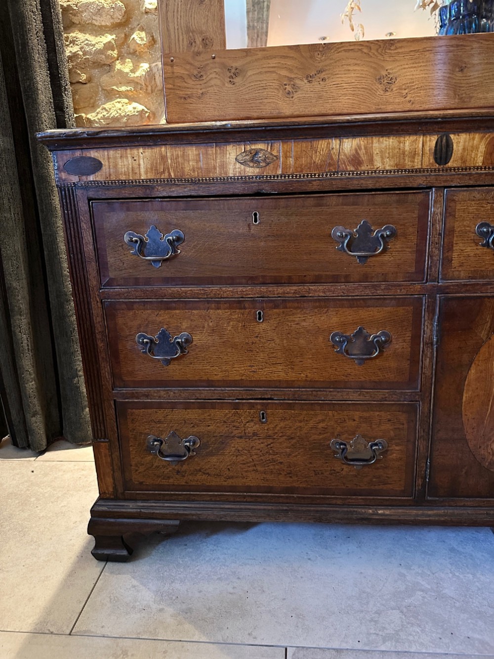 A Georgian oak Lancashire dresser base circa 1800 featuring drawer configuration, central cupboard doors with oval mahogany inlays, and brass handles. View III