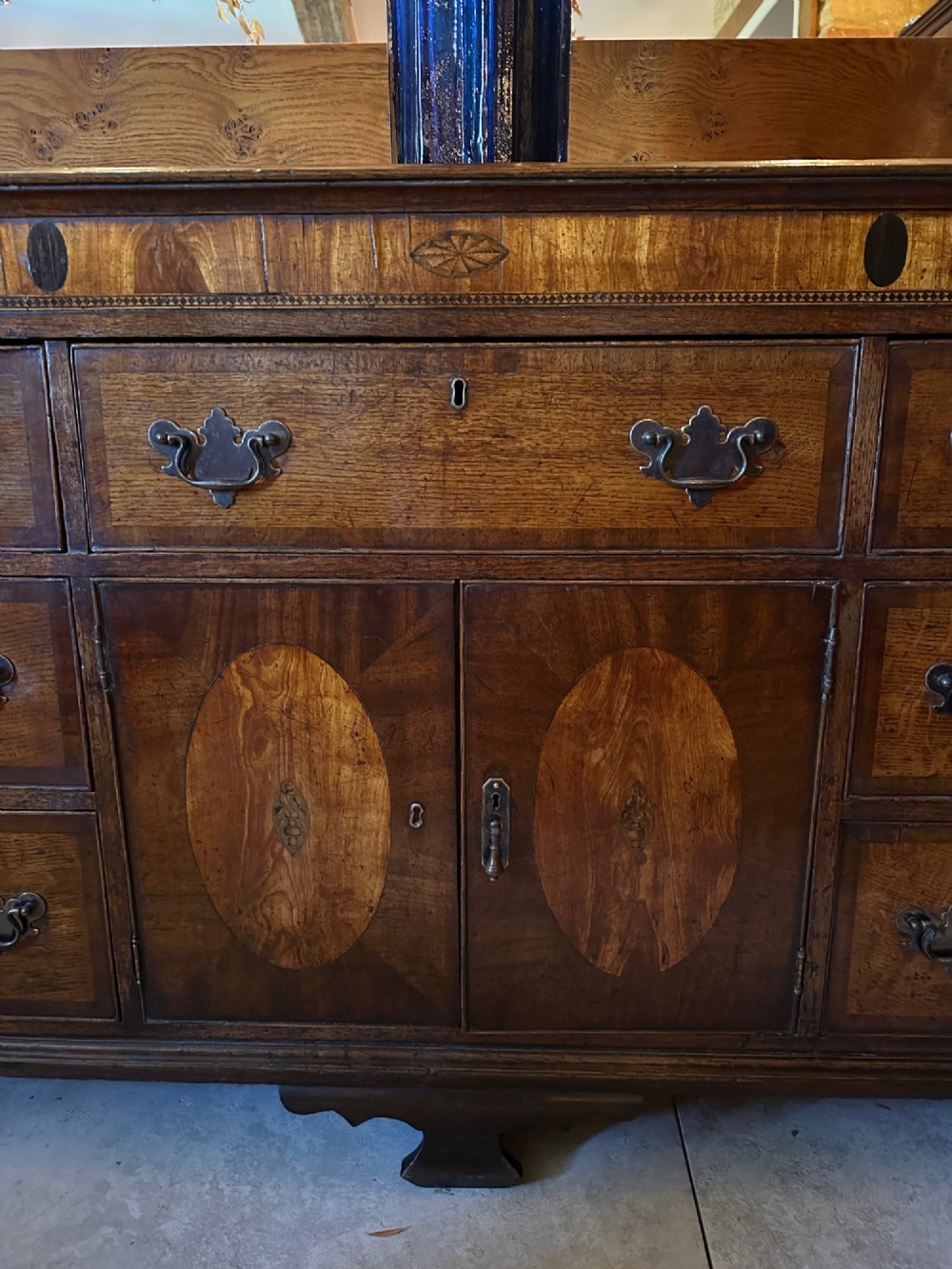 A Georgian oak Lancashire dresser base circa 1800 featuring drawer configuration, central cupboard doors with oval mahogany inlays, and brass handles. View IV